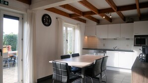 A modern kitchen with white cabinets, a wooden ceiling, and a dining area with a table and chairs.