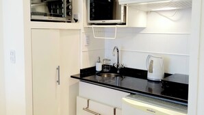 A compact kitchen with white cabinetry, a black countertop, a microwave, a kettle, and a trash can. - Temporary Apart. Excellent location in the historic center of Cordoba! One bedroom (Córdoba)
