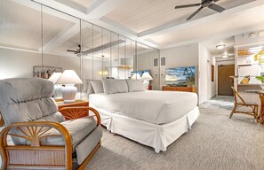 Una habitación de hotel moderna con una cama grande, un área de descanso con una silla, televisión y vista al mar.