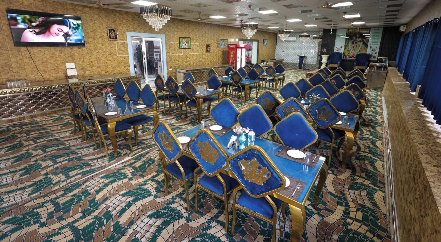 A banquet hall with rows of tables and chairs, a television screen, and a patterned floor.