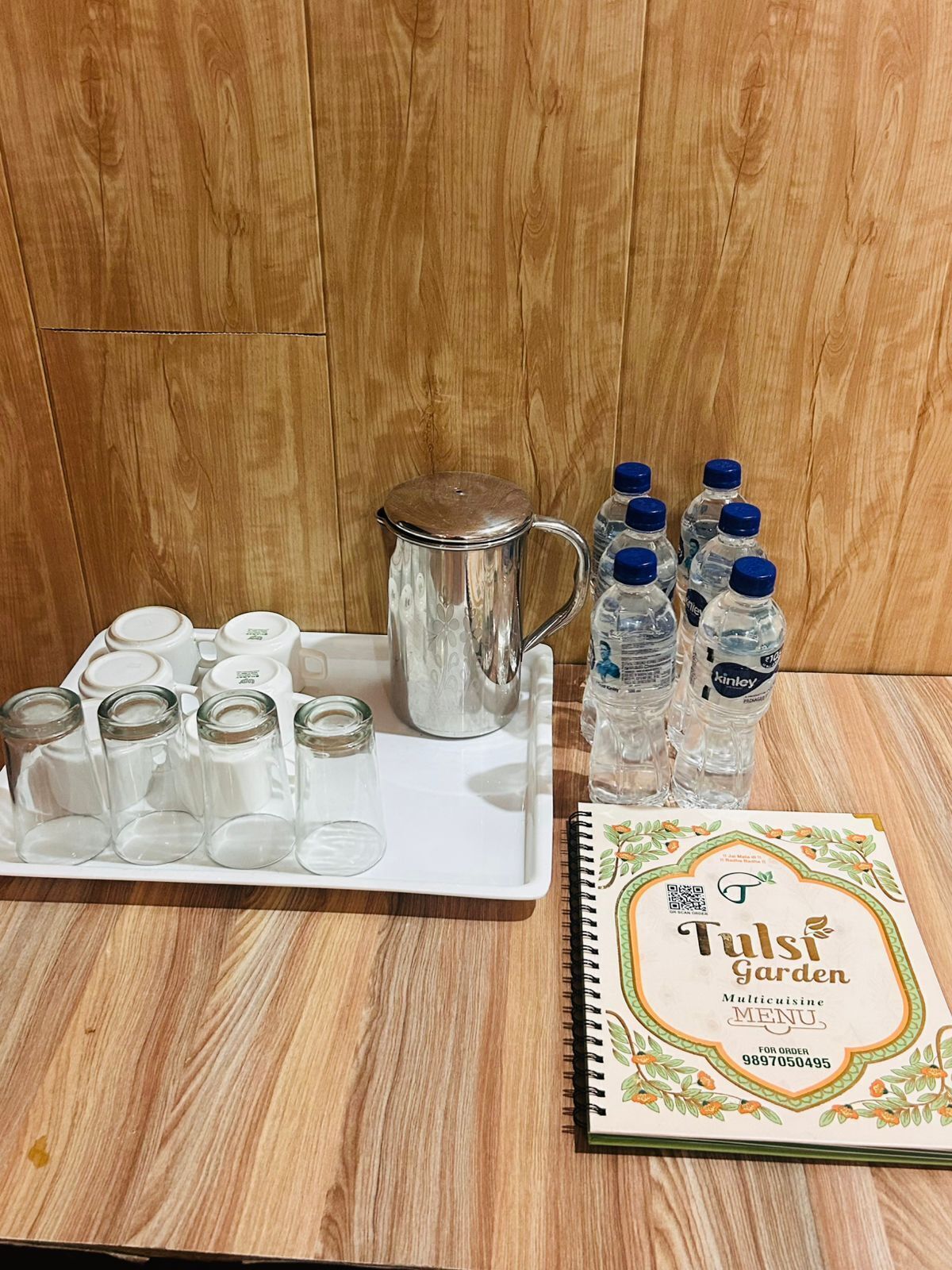 Una bandeja con una jeringa de metal, varios frascos de vidrio y botellas de agua sobre una superficie de madera.