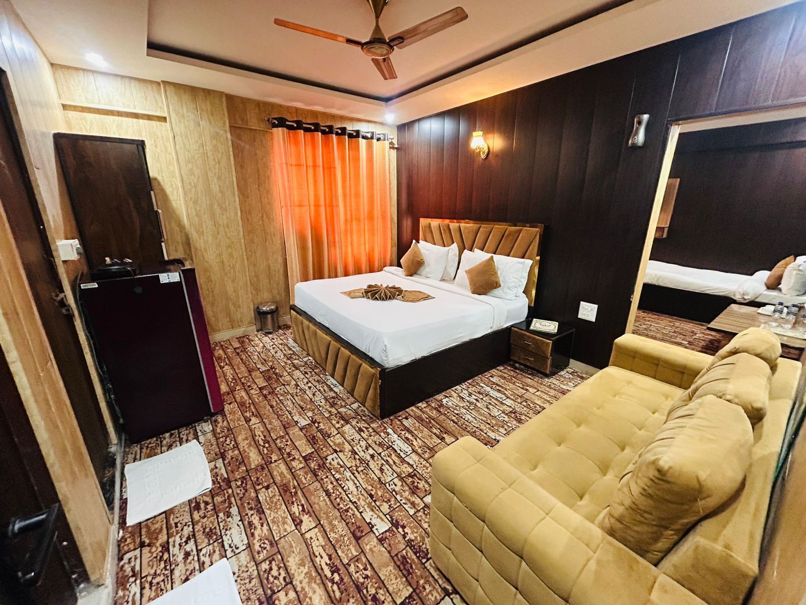 Habitación de hotel con cama, sofá, ventilador de techo, espejo y piso de madera.