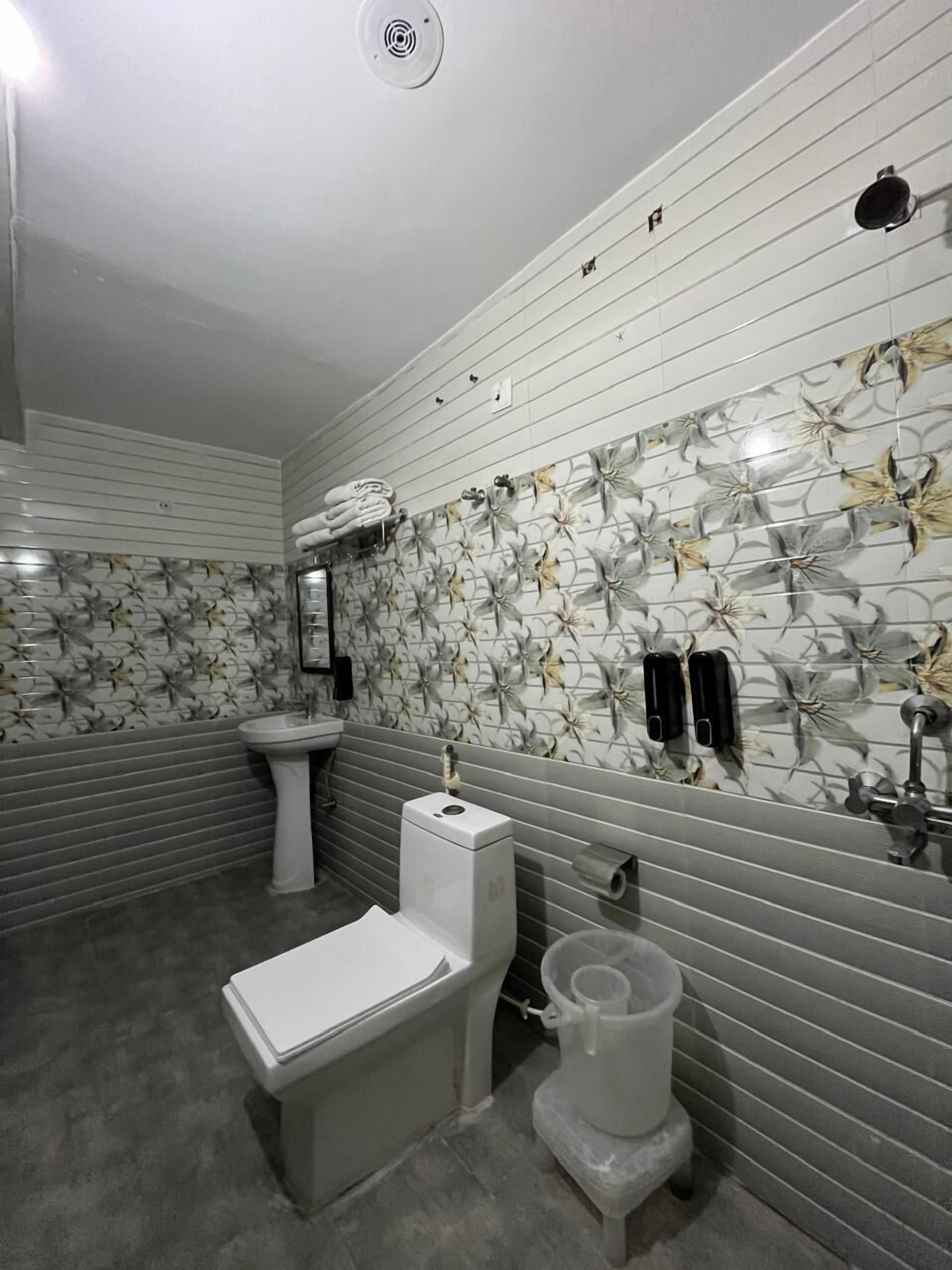 Une salle de bain comprenant des toilettes, un bidet et un lavabo. Les murs sont recouverts de carreaux décorés de motifs floraux.