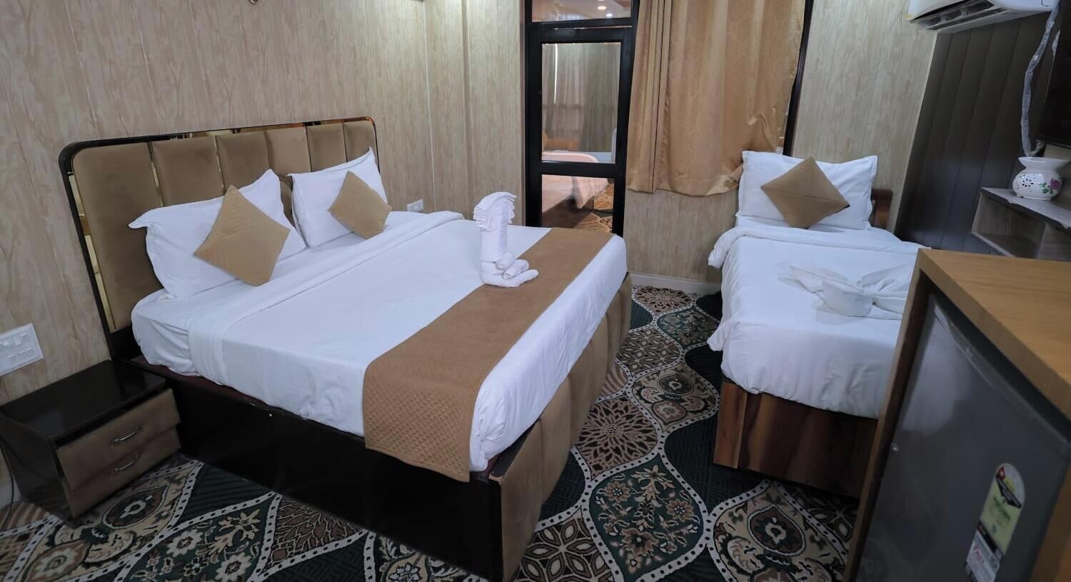 A hotel room with two beds, a nightstand, a desk, and a patterned carpet.