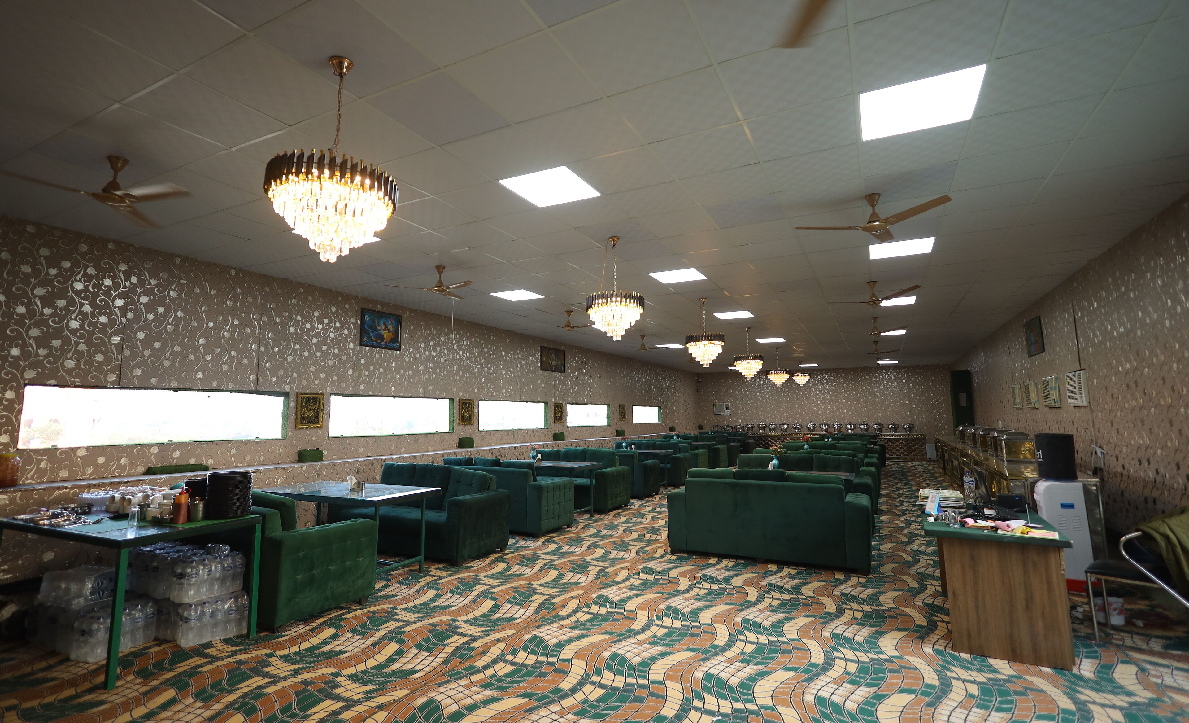 A conference room with green upholstered chairs, a patterned carpet, ceiling fans, and chandeliers.