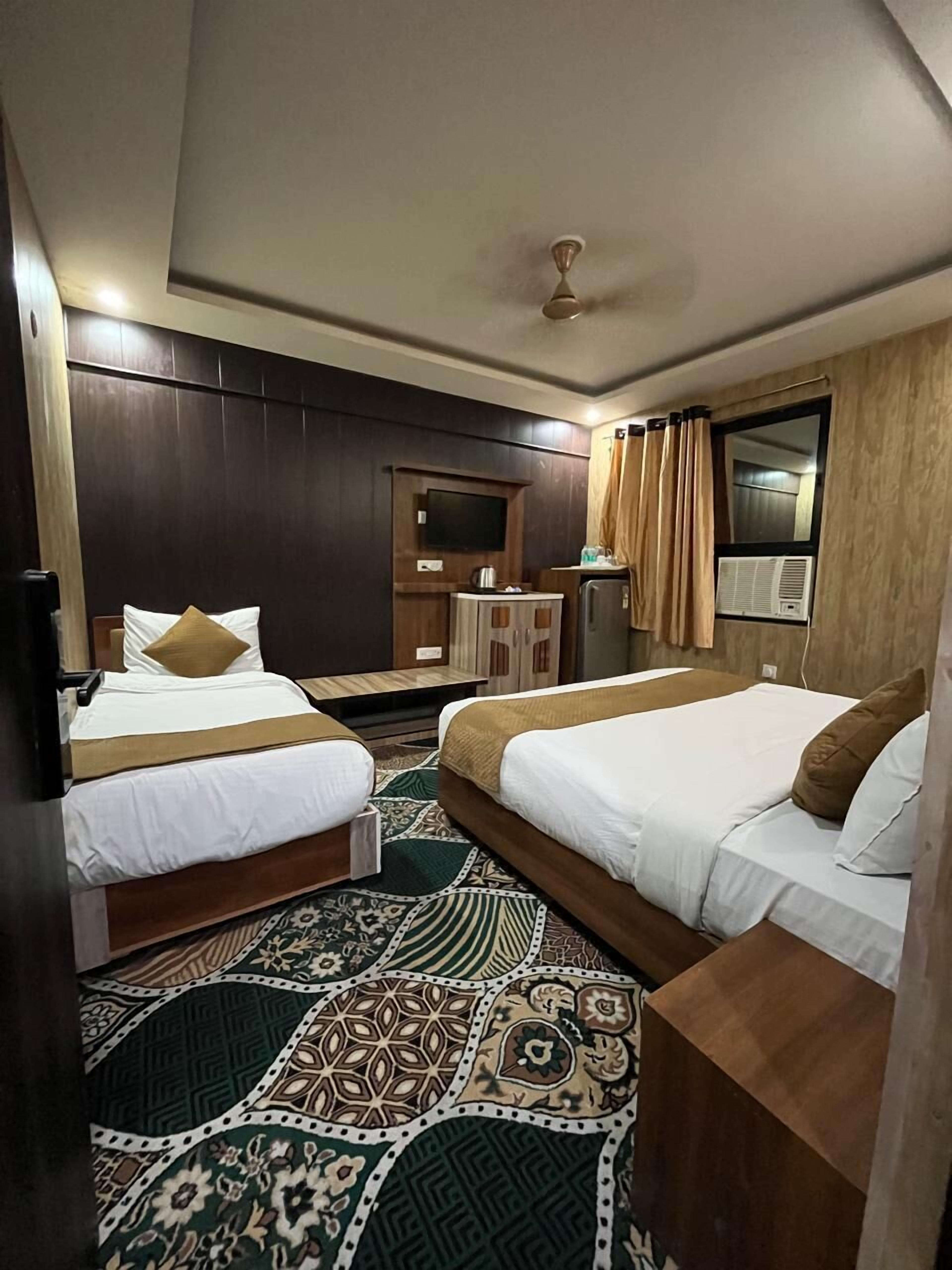 A hotel room with two beds, a TV, a small table, and a window with curtains.