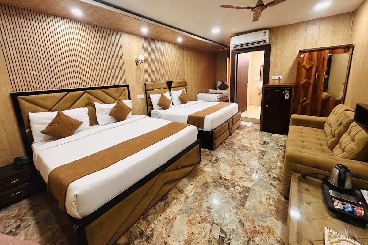 A hotel room with two beds, a sofa, a coffee table, a ceiling fan, and an air conditioning unit.
