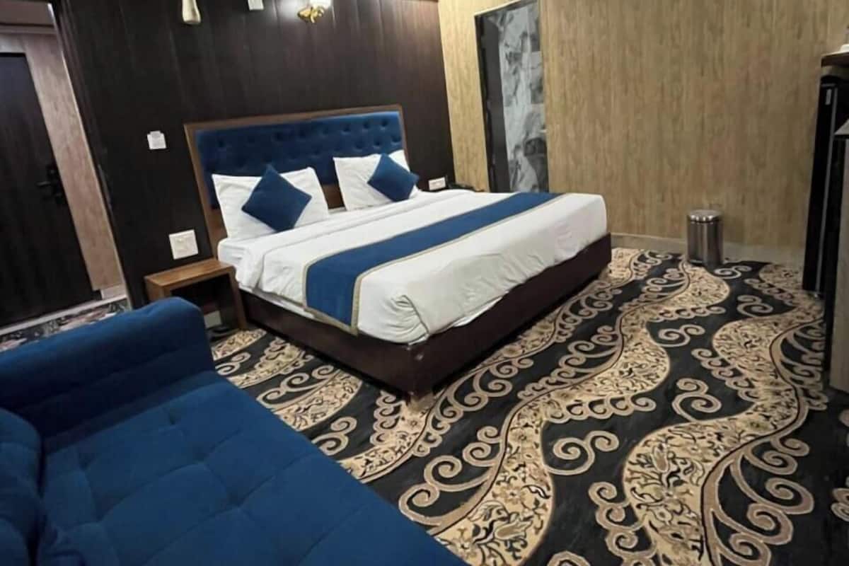 A hotel room with a bed, a blue sofa, a patterned carpet, and a ceiling fan.
