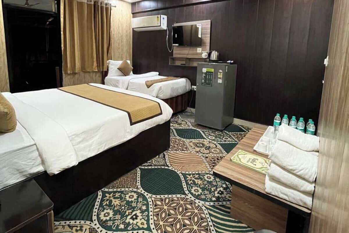 A hotel room with two beds, a desk, a refrigerator, and a ceiling fan.