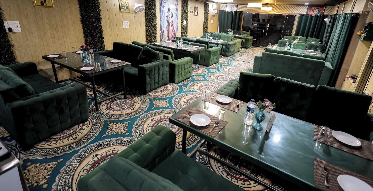 A restaurant with green upholstered seating, patterned carpet, and a variety of table settings.