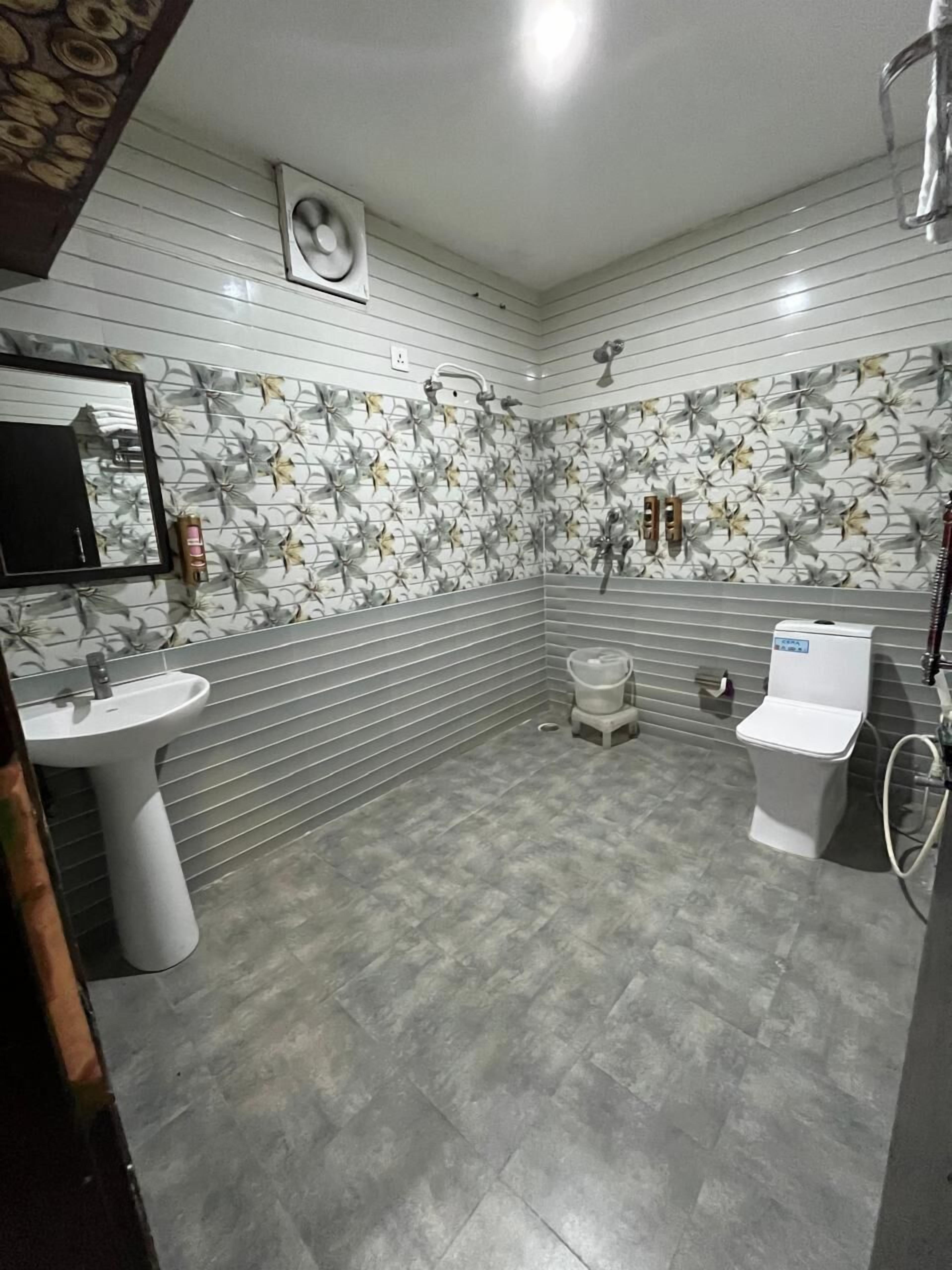 A bathroom with a white sink, toilet, and bidet, a mirror, and a shower with a fan.