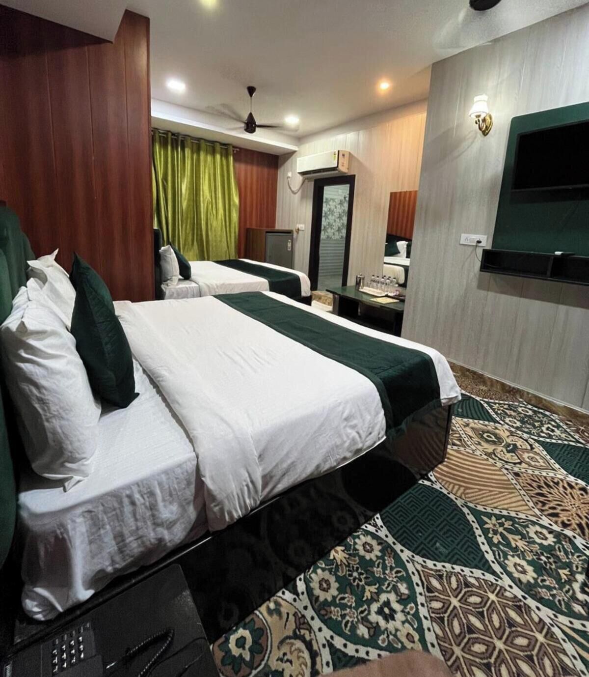 A hotel room with two beds, a desk, a television, and a patterned carpet.