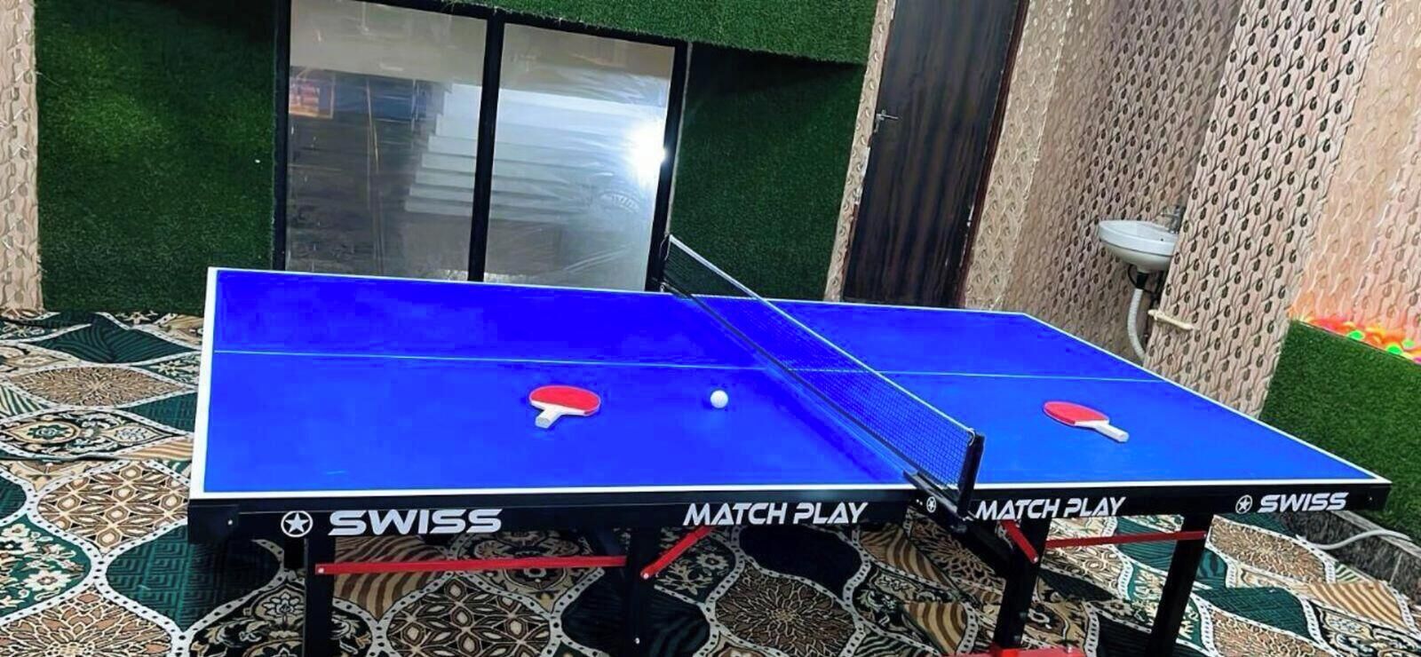 A ping pong table with a blue playing surface and red paddles, labeled "SWISS MATCH PLAY."