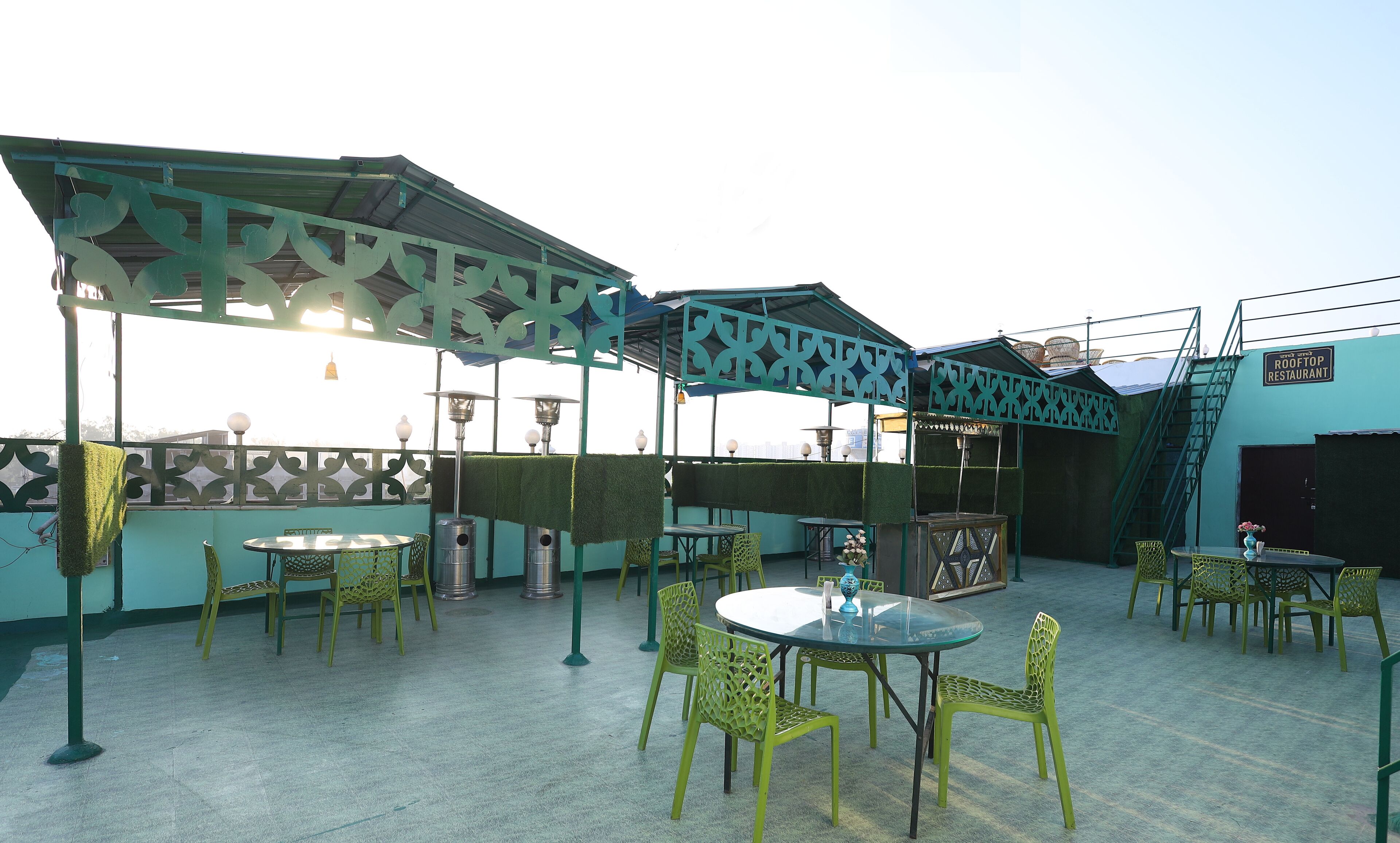 An outdoor seating area with green chairs and tables, a covered section with patterned metal railings, and a sign indicating a rooftop restaurant.