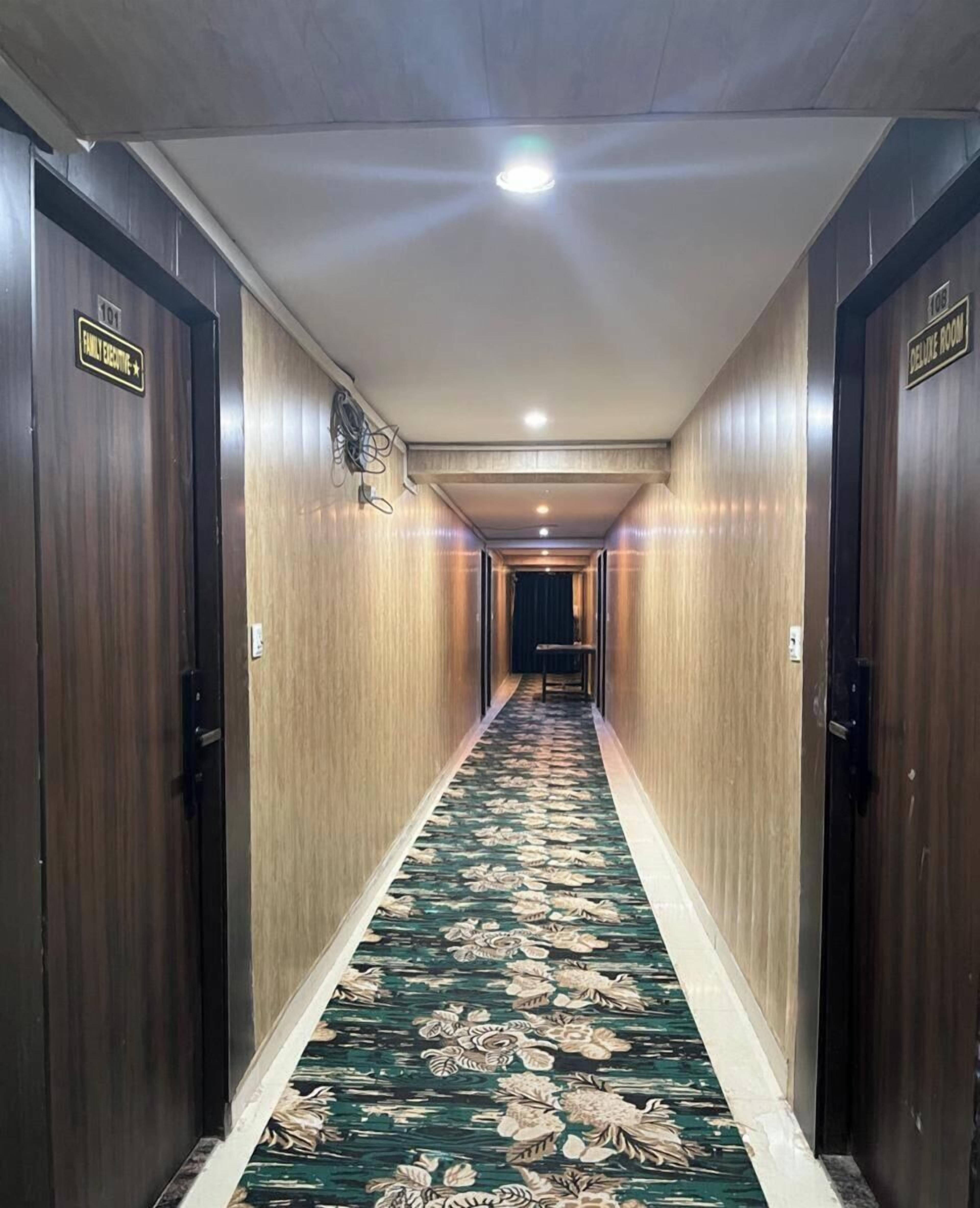A hotel hallway with wooden walls, a floral carpet, and doors labeled "Family Executive" and "Deluxe Room".