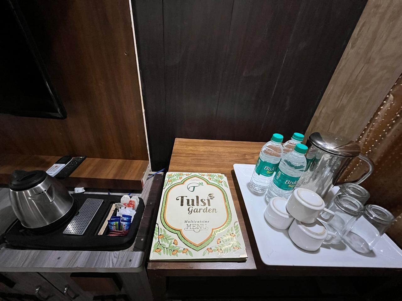 A kitchen area with a coffee maker, a menu, water bottles, and various containers on a table.