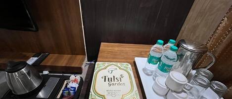 A kitchen area with a coffee maker, a menu, water bottles, and various containers on a table.