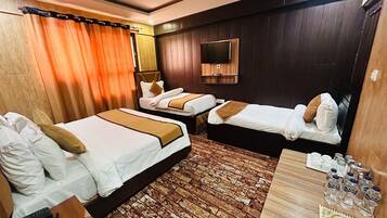 Ein Hotelzimmer mit zwei Betten, einem Fernseher, einem Holzboden und einem Tisch mit Wasserflaschen und einem Notizblock.