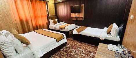 A hotel room with two beds, a TV, a wooden floor, and a table with water bottles and a notepad.