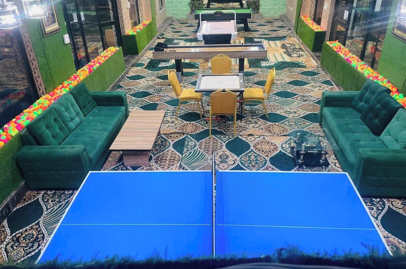 Una habitación con sofás verdes, una mesa de ping pong y una alfombra estampada.