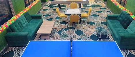 A room with green sofas, a ping pong table, and a patterned carpet.