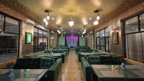 Un restaurante con asientos tapizados en verde, mesas de madera y lámparas colgantes.