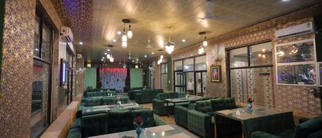 Un restaurante con asientos tapizados en verde, varias mesas y ventiladores de techo.