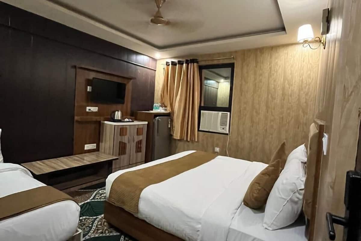 A hotel room with two beds, a desk, a television, and a window with curtains.