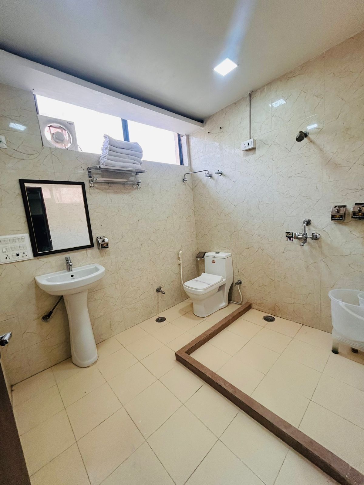 Een badkamer met een wastafel op een voetstuk, toilet, douche en een raam boven de wastafel.