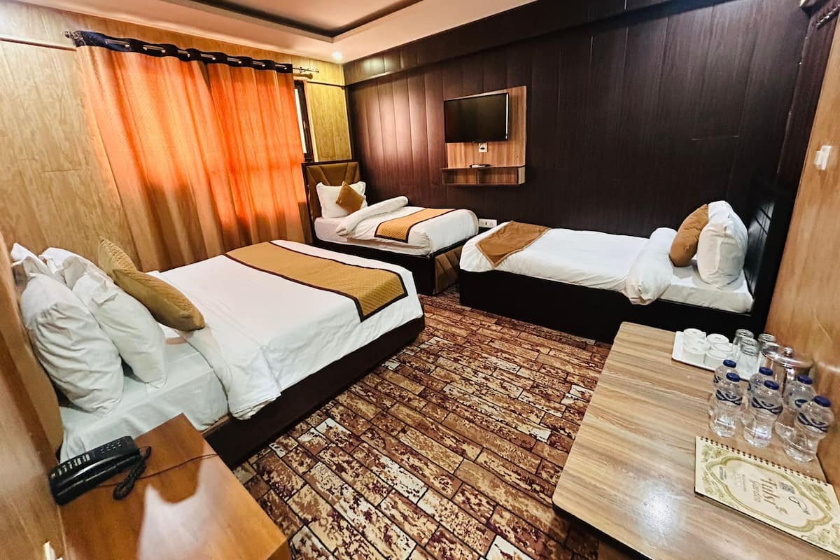 A hotel room with two beds, a TV, a wooden desk, and a patterned floor.
