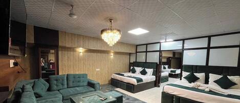 Une chambre d’hôtel avec un canapé d’angle, deux lits simples, un lustre et un grand miroir.