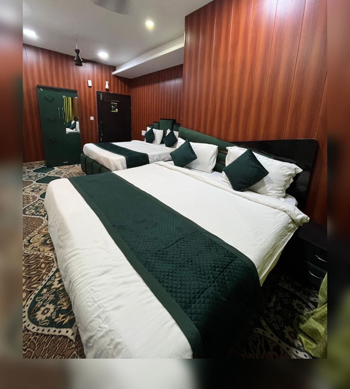 A hotel room with two beds, a green and white color scheme, wooden paneling, and a patterned carpet.
