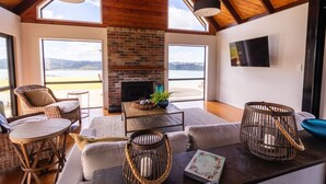 A spacious living area with a fireplace, wicker furniture, and large windows offering a view of the outdoors.