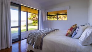A bedroom with a large bed, a view of a garden through a sliding door, and a window with blinds.