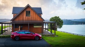 A modern house with a car parked in front, a covered porch, and a view of a lake and mountains.