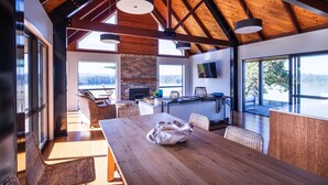A spacious dining area with a wooden table and chairs, a fireplace, and large windows offering a view of the outdoors.