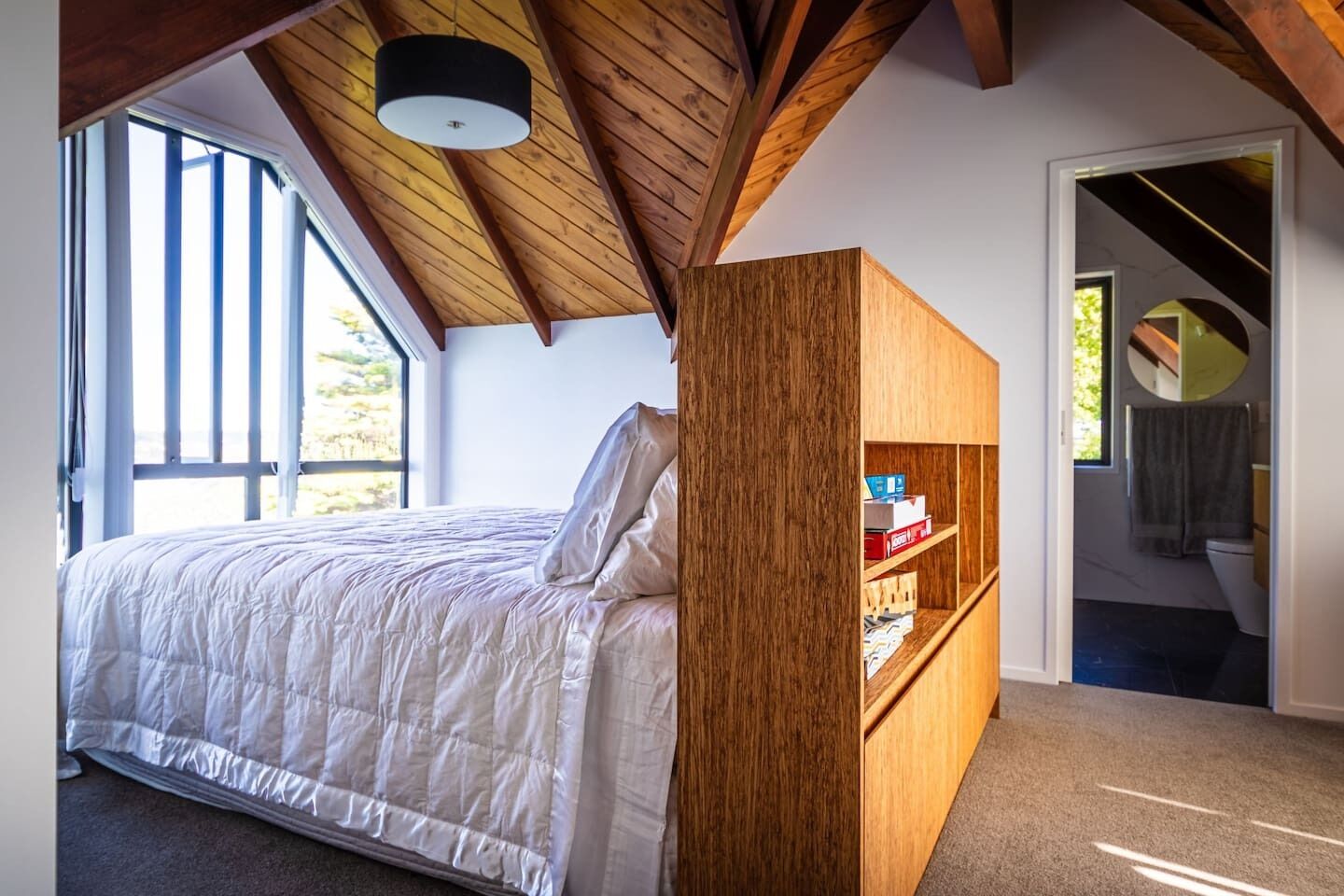 Een slaapkamer met een bed, een houten boekenkast en uitzicht buiten door een raam.