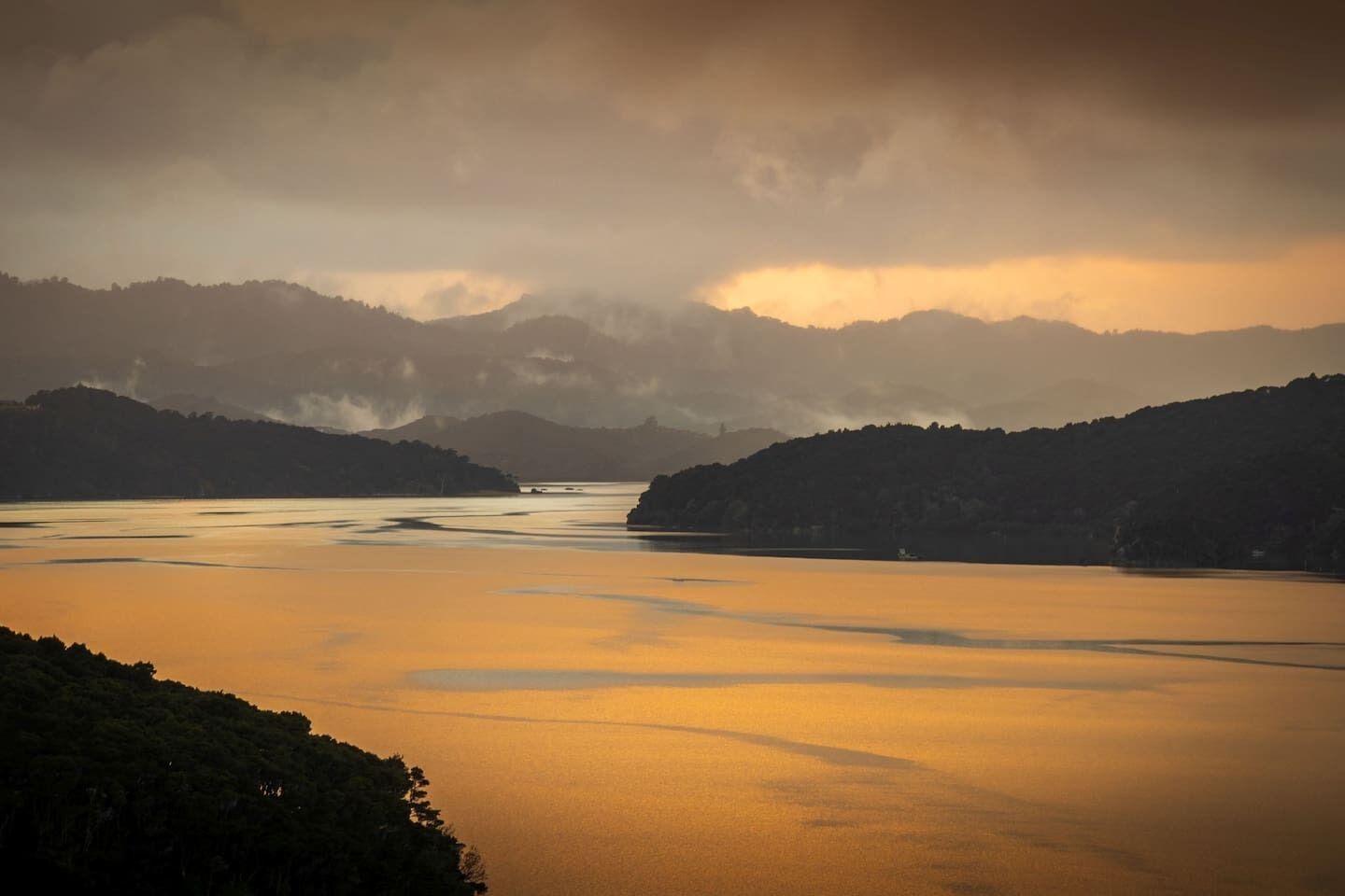 A panoramic view of a calm river with surrounding hills and a cloudy sky.