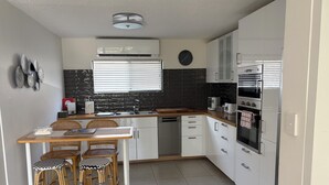 Eine kompakte Küche mit Essbereich, ausgestattet mit einer zentralen Kochinsel, weißen Schränken, einer schwarzen Küchenzeile und einem eingebauten Backofen.