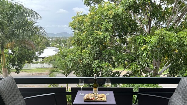 Ein Balkon mit zwei Stühlen, einem Tisch, einer Flasche, einem Glas und einem Teller mit Essen.
