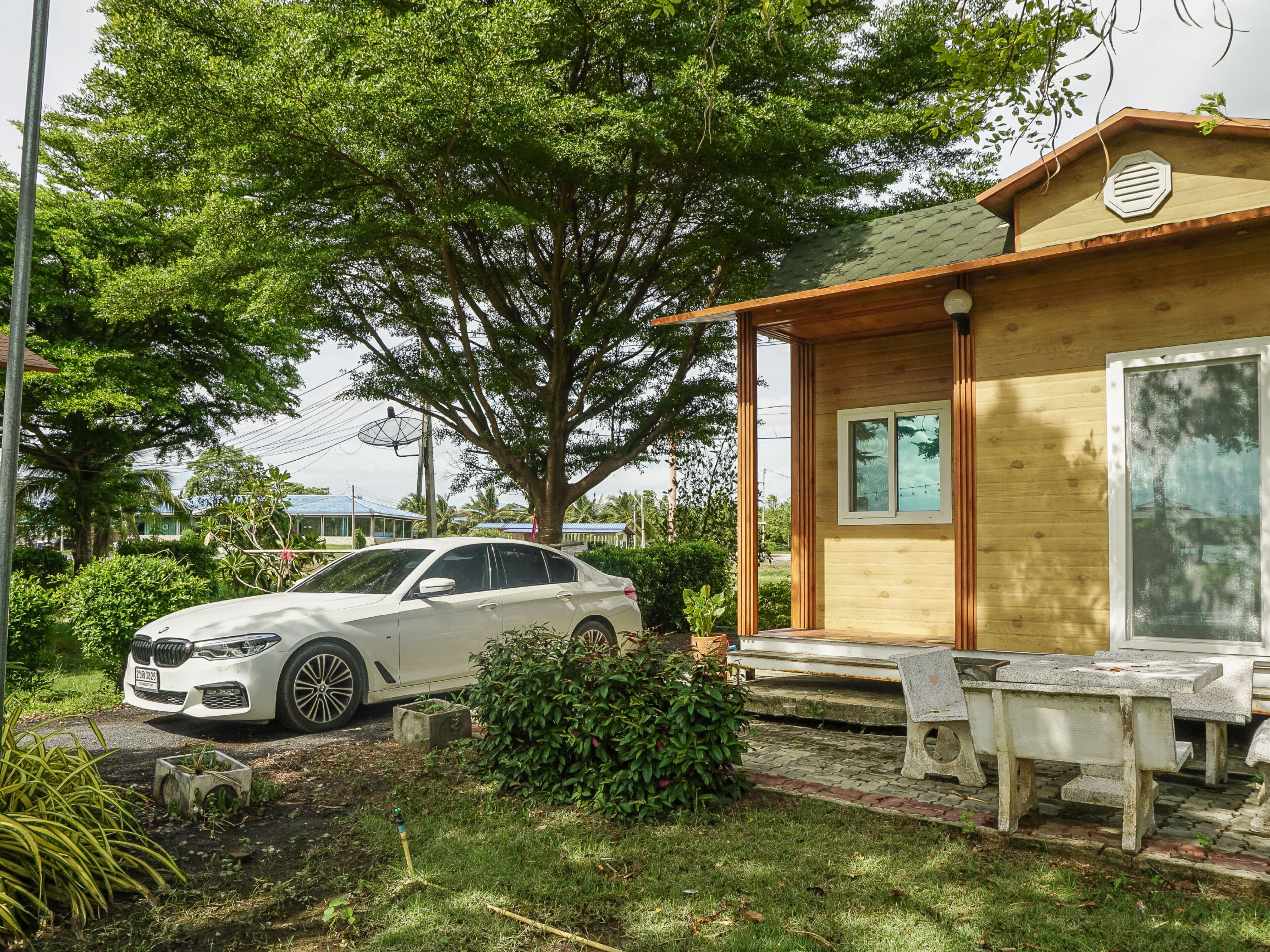 Un coche blanco aparcado frente a una casa de madera con un ventanal grande y un banco en el exterior.