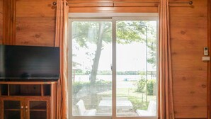 A room with a wooden interior, a sliding glass door leading to an outdoor area with a tree and seating. - Beung Sampathuan Nakornchaisri Resort (Nakhon Chai Si)