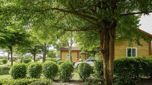 A building with a wooden exterior and a window, surrounded by well-maintained bushes and trees. - Beung Sampathuan Nakornchaisri Resort (Nakhon Chai Si)