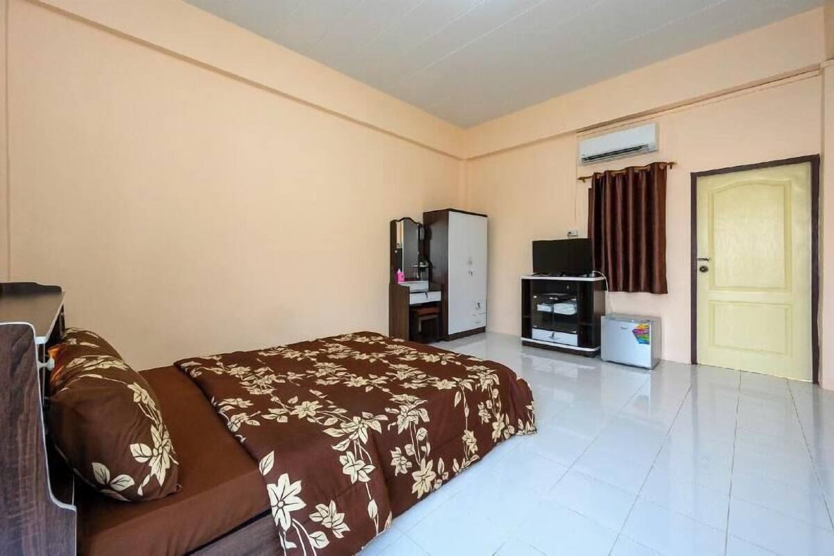 A hotel room with a bed, a wardrobe, a television, an air conditioning unit, and a door.