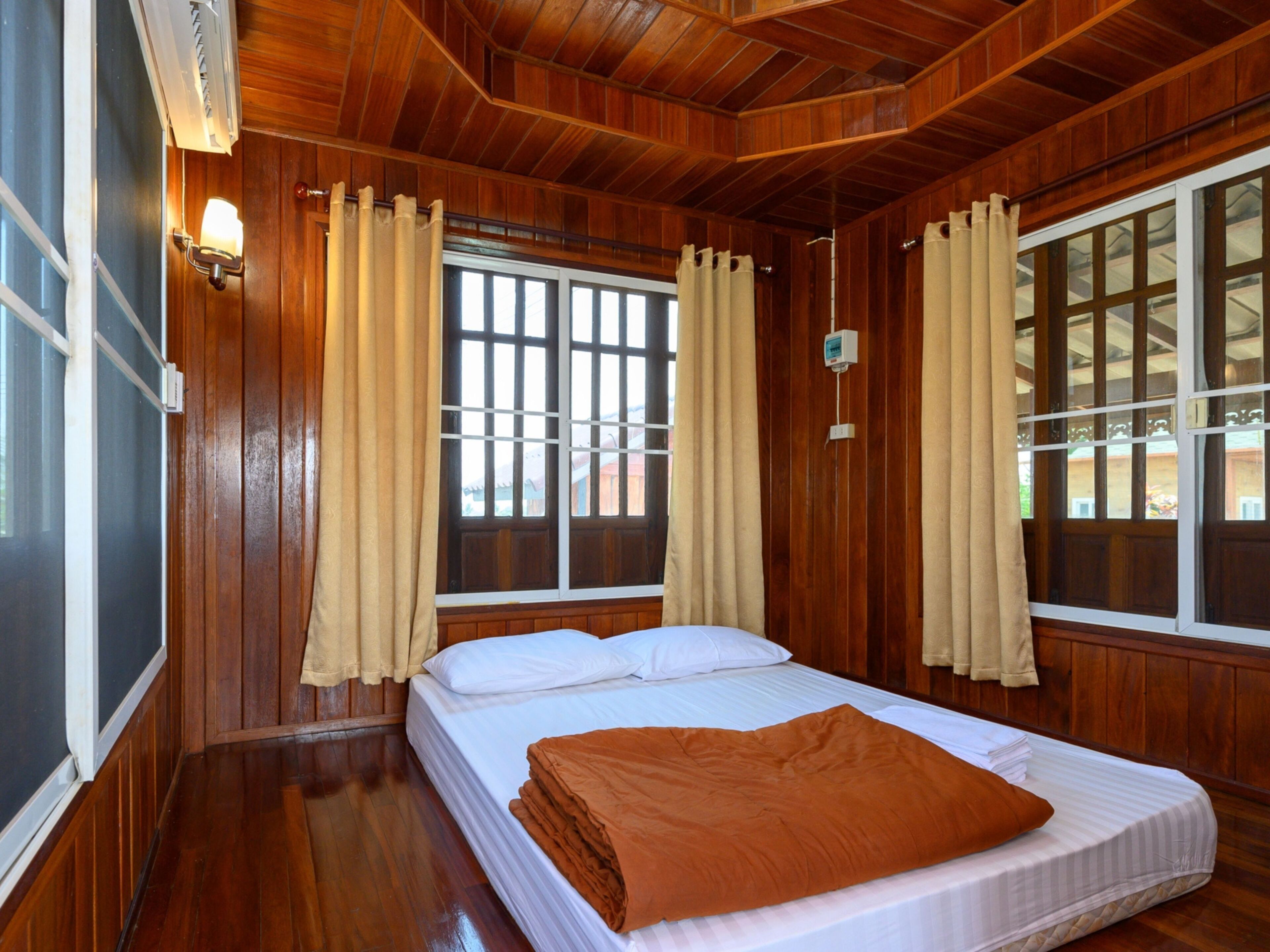 A room with wooden paneling, a bed with white bedding, and two windows with curtains.