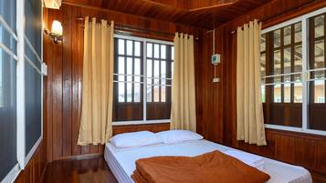 A room with wooden paneling, a bed with white bedding, and two windows with curtains.
