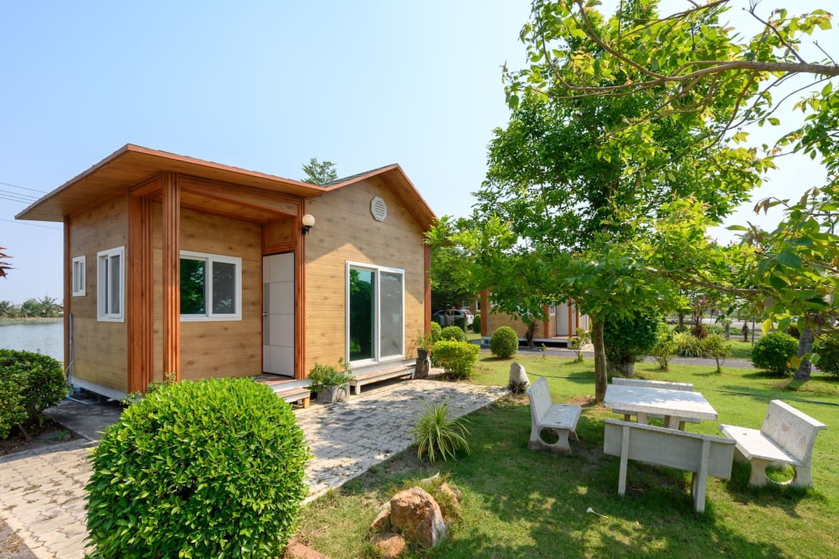 A small wooden house with a paved entrance, surrounded by a well-maintained lawn and a few potted plants.