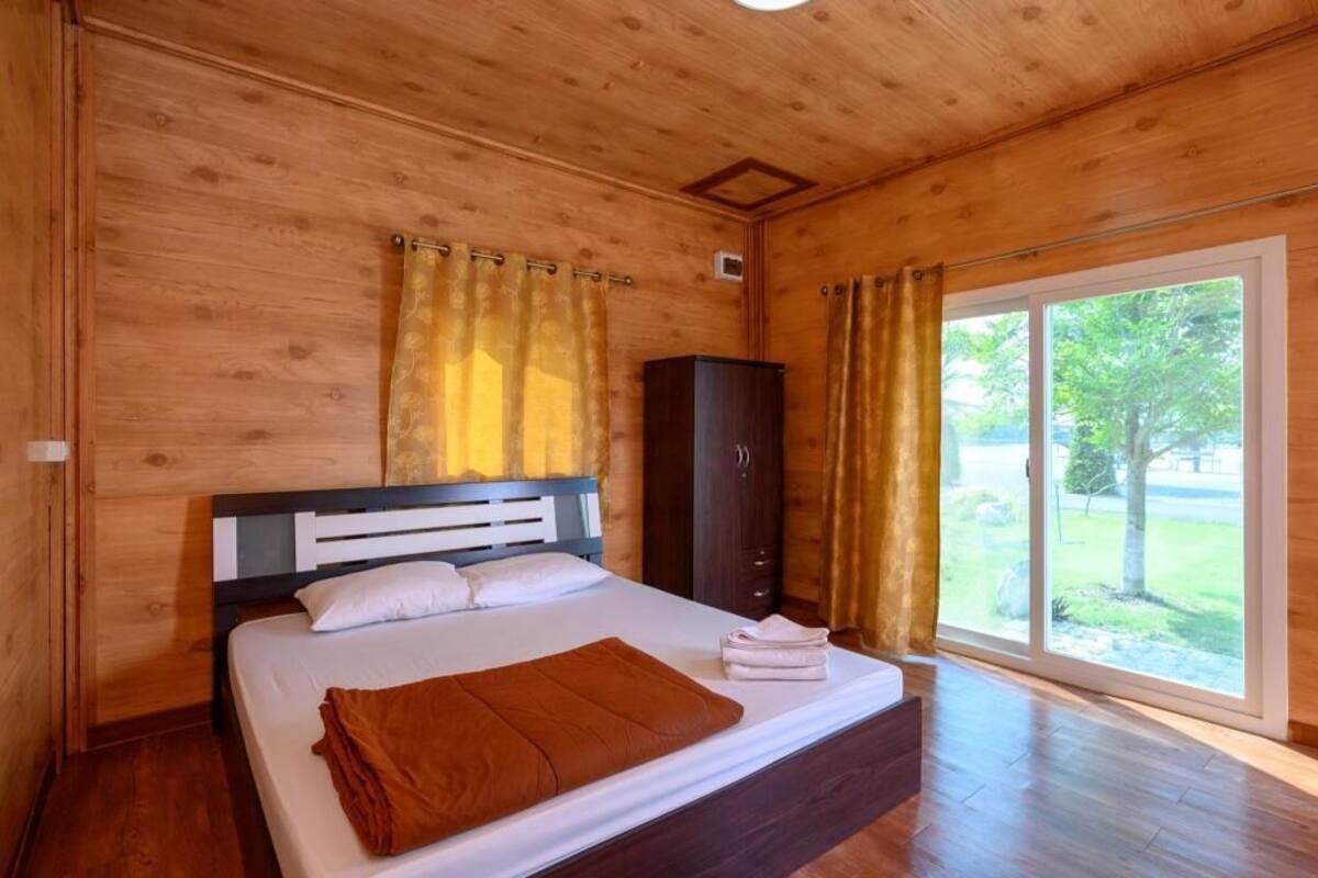 A wooden-paneled bedroom with a bed, a wardrobe, and a sliding glass door to a garden.
