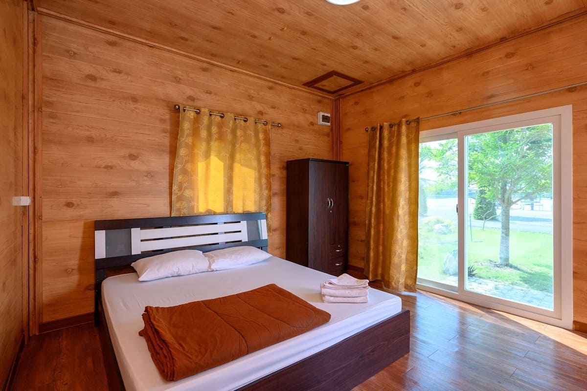 A wooden-paneled room with a bed, a wardrobe, and a large window.