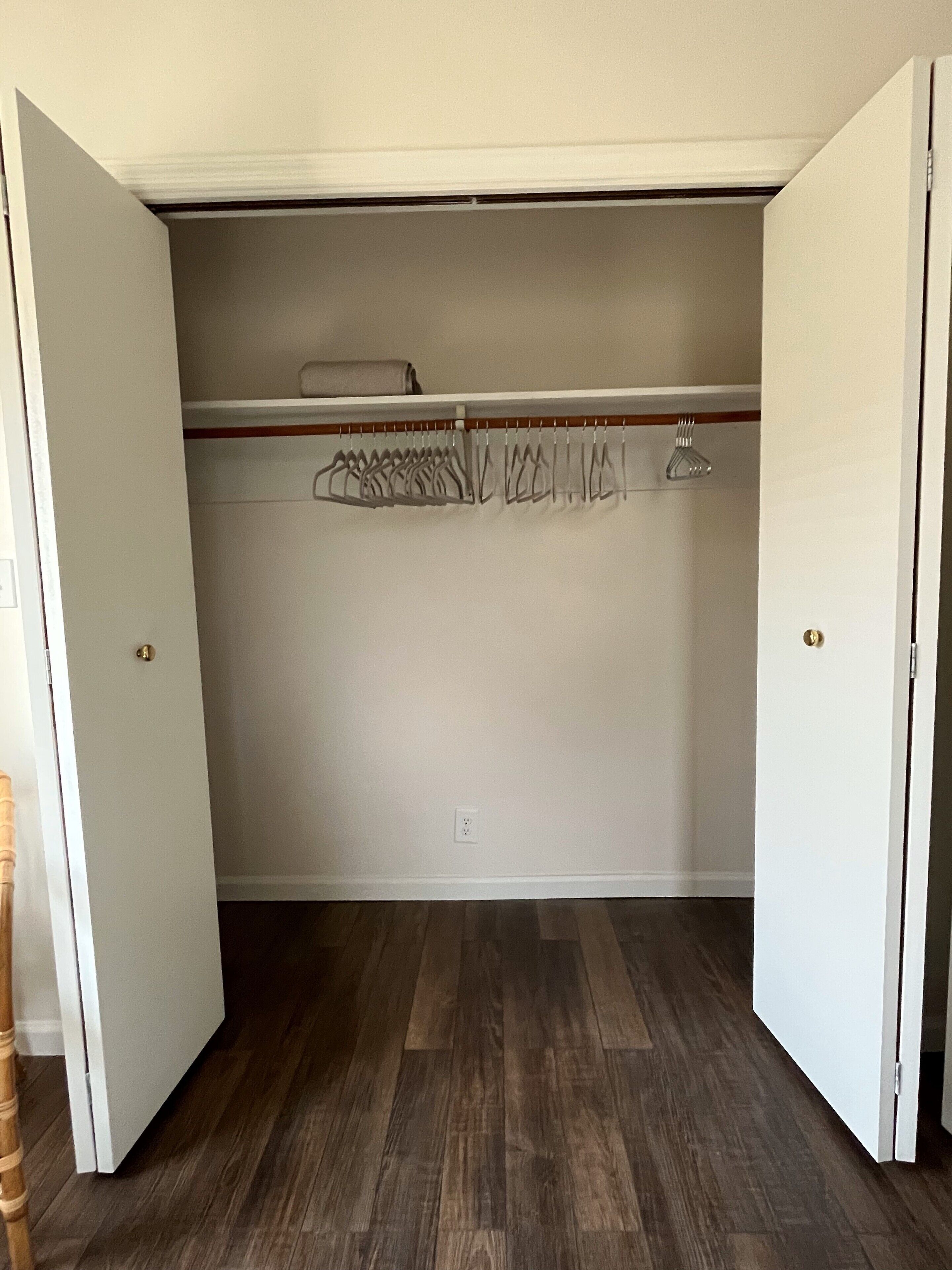 Een inloopkast met houten vloer, een kledingroede en een opgevouwen voorwerp op de bovenste plank.